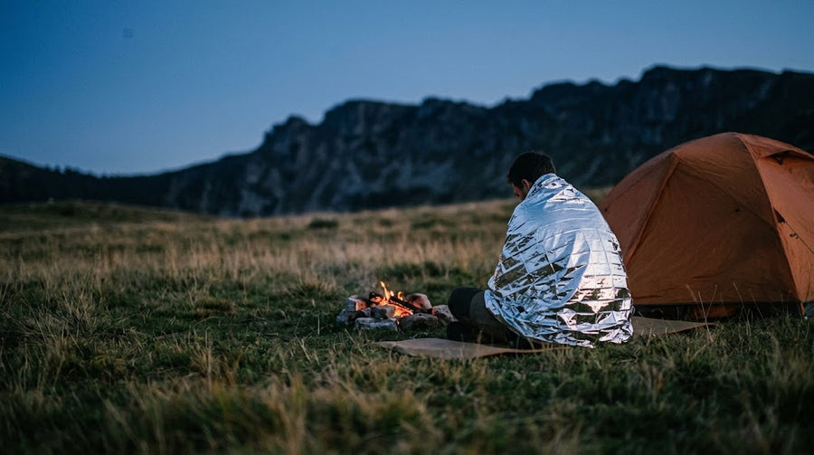 Bivouac au crépuscule en montagne, couverture de survie sur les épaules près d'un feu