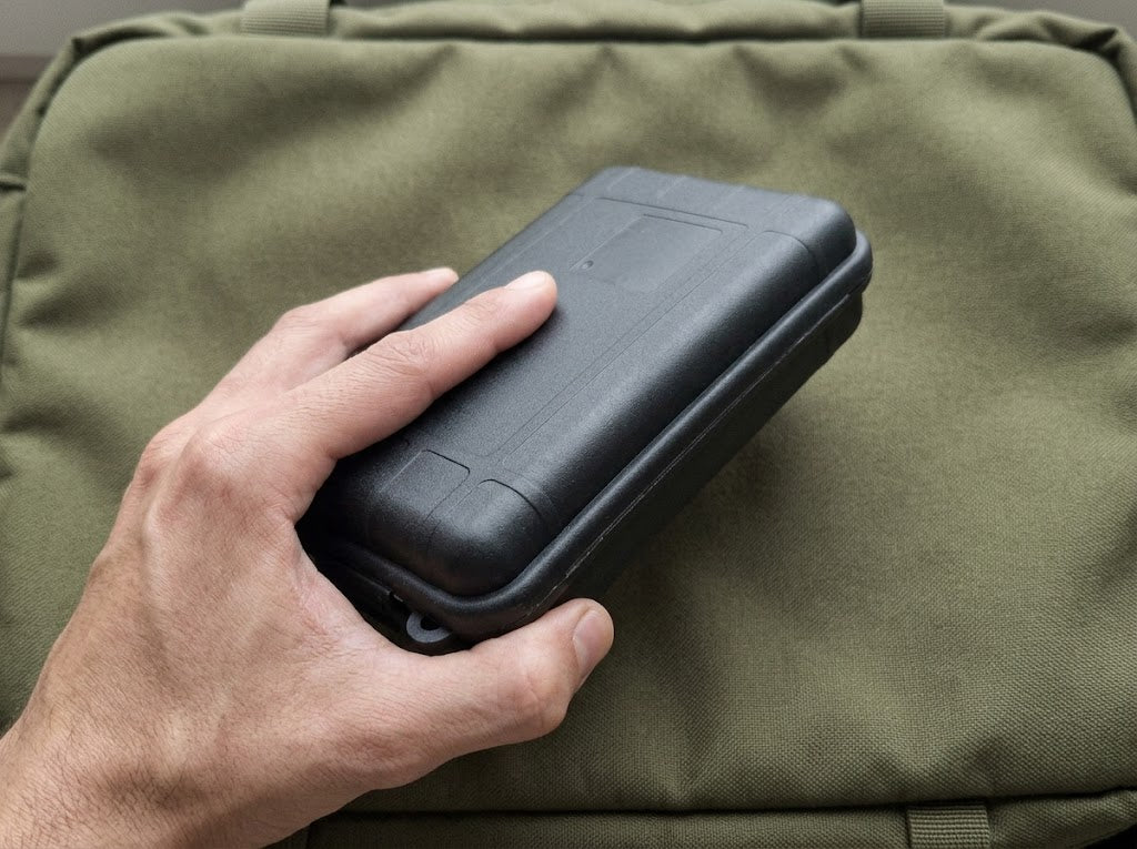 Étui fermé du kit de survie Ultime Survie tenu dans une main, posé sur un sac à dos